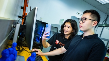 A male and female student, both wearing black shirts look at a computer monitor. 3D printed human objects in blue are in the foreground.