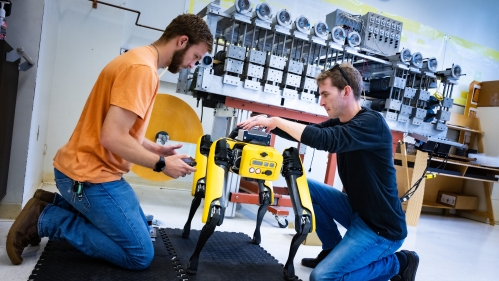 Two male college students work with a robotic dog in a lab.