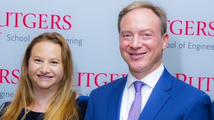 Female with long blonde hair and male wearing a blue suit, white shirt, and purple standing in front of Rutgers School of Engineeirng step-and-repeat banner. ing