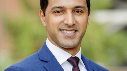 Headshot of smiling male wearing a blue suit, shite shirt, and maroon tie