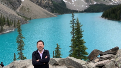 male standing on rocky mountain with blue lake and mountains in the backgroung