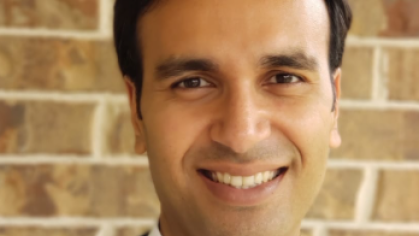 Head shot of male with black hair, dark suit jacket and open neck white shirt.