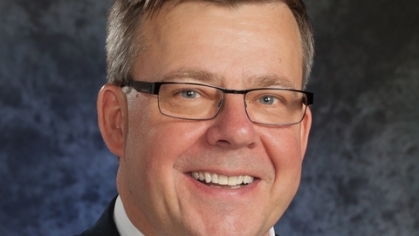 Head shot of white male wearing a dark suit with a white shirt and red tie.