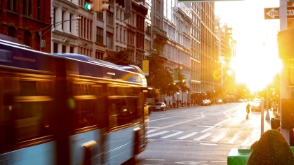 NYC bus driving through the intersection of 23rd Street and 5th Avenue with the sunset shining between the skyline buildings 