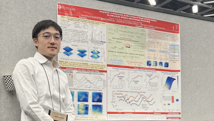 Male student with black hair wearing a white shirt and dark slacks, stands next to a research poster.