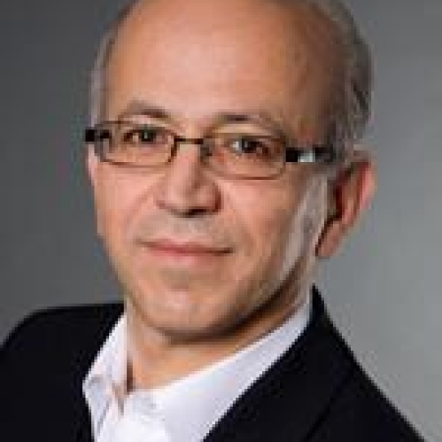 headshot of male short grey hair with eyeglasses and wearing a black suit jacket and white button down shirt