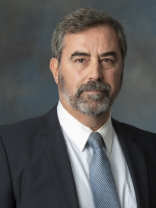 Headshot of white male with a beard wearing a dark suit, shite shirt, and blue tie