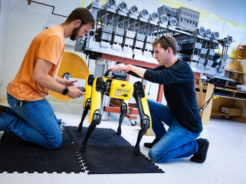 Two male college students work with a robotic dog in a lab.