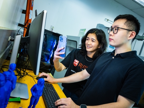 Female and male college student look at computer screen. Blue 3D figures are in the foreground.