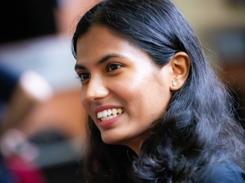 Female graduate student smiles as she looks to the left. She has black hair and is wearing a black shirt.