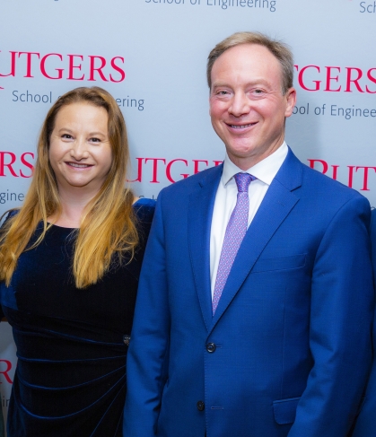 Female with long blonde hair and male wearing a blue suit, white shirt, and purple standing in front of Rutgers School of Engineeirng step-and-repeat banner. ing