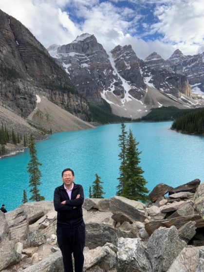 male standing on rocky mountain with blue lake and mountains in the backgroung