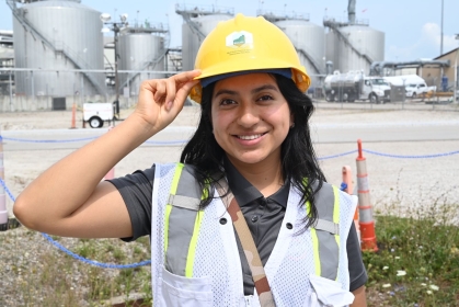 Young female with long black hair wearing a yellow hard hat and safety vest.