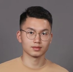 Headshot of Asian male with short black hair, wearing eyeglasses and a tan shirt.